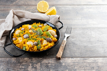 Traditional Valencian paella with rabbit, chicken, garrofon beans, snails, Moroccan green beans and saffron on wooden table. Copy space