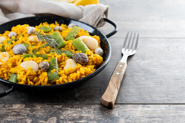 Traditional Valencian paella with rabbit, chicken, garrofon beans, snails, Moroccan green beans and saffron on wooden table. Copy space