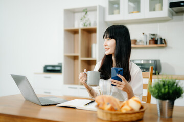 Woman using laptop while sitting at home. Young woman sitting in kitchen