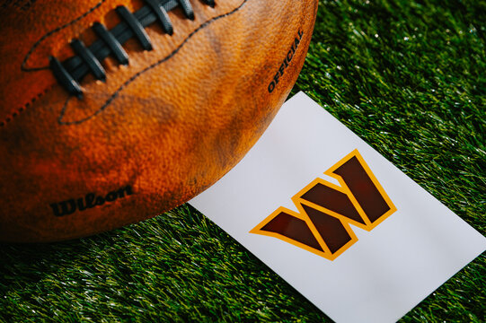 Washington Commanders american football team Logo and American football ball on Green Grass.