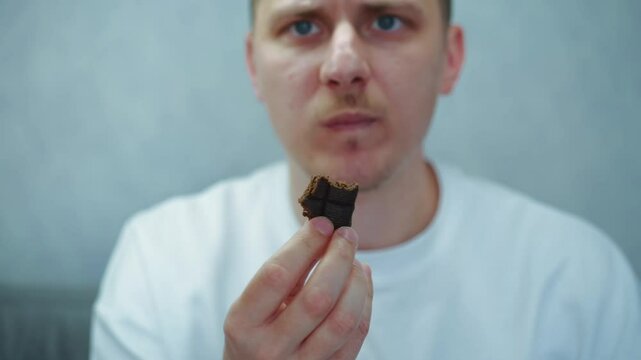 Young European man in a white T-shirt eats dark chocolate in front of the camera.Man bites and chews a chocolate bar.Chocolate, dessert, energy, sweetness, milk