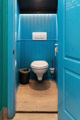 a bathroom with a white toilet, bright blue wood paneling, and a trash can.