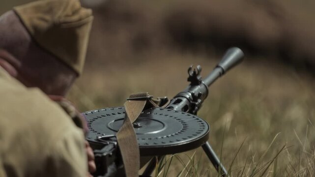 Soviet Red Army soldier with Degtyaryov light machine gun lies in grass field. Battle scene from Great Patriotic War time in USSR. Historical reconstruction event. World war II period. Defense. Summer