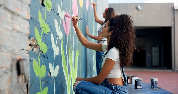 Girl, teamwork or artists painting on wall for mural, drawing flowers or community service at building. People, creative or women with brush for floral decoration, renovation or project for design