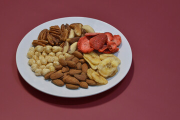 A variety of nuts and dried fruits on a plate on red background. Hazelnuts, pecans, brazil nuts, almonds, dried strawberries and bananas. The concept of nutrition, diet, healthy eating and sports