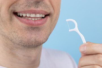 Man brushing teeth with toothpick with dental floss on blue background