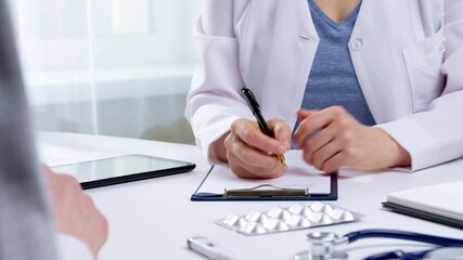 Hands doctor writes a prescription and consults a patient sitting at the table. Medical care in the clinic. - Powered by Adobe