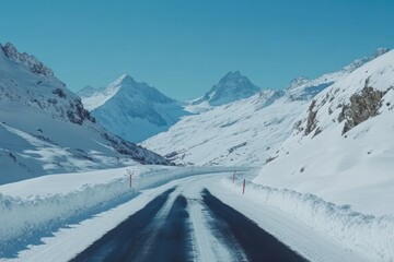 Scenic view of a snowy asphalt road winding through majestic alpine mountains under a clear blue sky