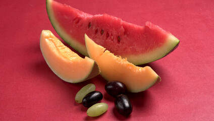Natural organic juicy sliced of melon and watermelon with different types of grapes on a red...