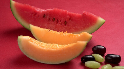 Natural organic juicy sliced of melon and watermelon with different types of grapes on a red background. Slices are on the table. top view, Agriculture concepts.