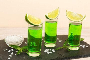 Fototapeta premium Sweet refreshing mint liqueur, with ice and mint leaves on table background, Shots with lime slice and mint flat lay