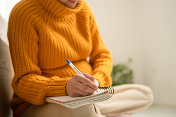 Expecting mother thoughtfully writing important delivery notes in her journal. Warm domestic scene...