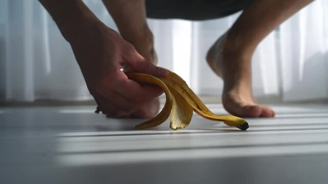 Throwing a banana peel on the floor.
Picking up trash from the floor.
A yellow banana on a white floor in a bright room.
A man throws away a banana peel.
A man ate a ripe banana