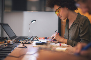 Young woman soldering a circuit boards in her tech office