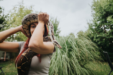 A confident girl holding a large snake in a green outdoor setting. The intimate interaction...