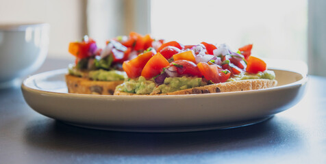 Close-up of fresh avocado toast topped with sliced tomatoes, capers, and parsley, served on a white plate. The dish looks vibrant and delicious, perfect for a healthy breakfast 