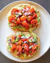 Close-up of fresh avocado toast topped with sliced tomatoes, capers, and parsley, served on a white plate. The dish looks vibrant and delicious, perfect for a healthy breakfast 