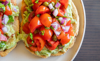 Close-up of fresh avocado toast topped with sliced tomatoes, capers, and parsley, served on a white plate. The dish looks vibrant and delicious, perfect for a healthy breakfast 