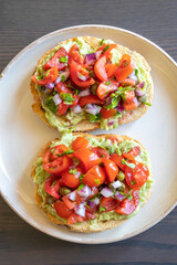 Close-up of fresh avocado toast topped with sliced tomatoes, capers, and parsley, served on a white plate. The dish looks vibrant and delicious, perfect for a healthy breakfast 