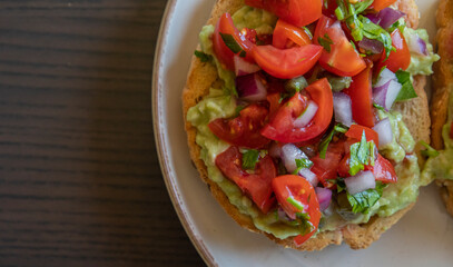 Close-up of fresh avocado toast topped with sliced tomatoes, capers, and parsley, served on a white plate. The dish looks vibrant and delicious, perfect for a healthy breakfast 