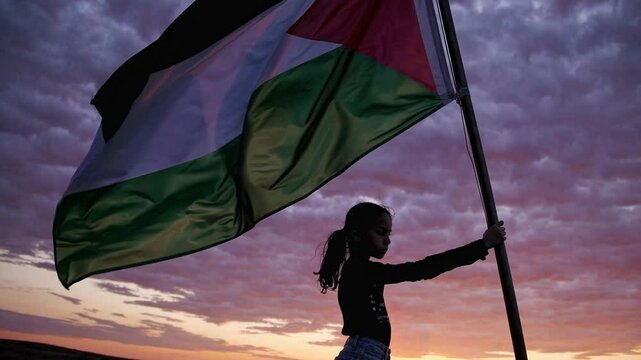Young girl holding Palestinian flag against sunset sky