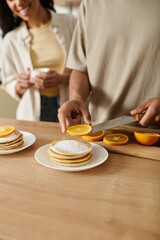 Loving couple shares a cozy morning at home while preparing pancakes with fresh oranges