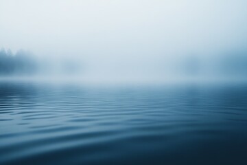 Obraz premium A misty, serene lake stretches into the distance, shrouded in a translucent fog that blurs the horizon and creates a tranquil atmosphere.