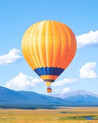 Fototapeta premium A vibrant orange hot air balloon soars over a scenic landscape of mountains and plains under a clear blue sky