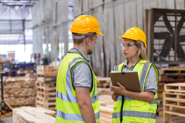 Workers wearing safety uniform and yellow hard hat working holding clipboard checking quality of wooden products at workshop manufacturing. man and woman worker wood warehouse industry.