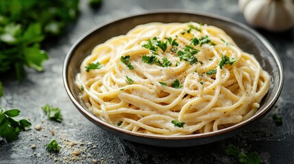Creamy Alfredo spaghetti pasta dish served in a black bowl garnished with fresh parsley on a rustic dark surface with herbs and garlic in the background