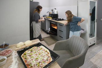 Attractive daughter cooking pizza with her mother in the kitchen