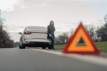 Businesswoman making phone call near broken car with warning triangle