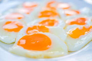 Close up of multiple sunny-side-up eggs with vibrant orange yolks and glossy whites, freshly cooked and arranged on a white plate, perfect for breakfast or food related concepts