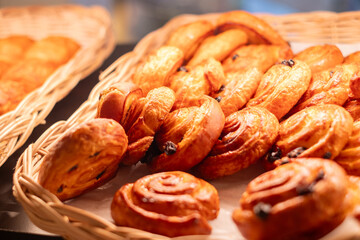 Freshly baked raisin danishes and pastries arranged in a wicker basket, showcasing golden brown texture and inviting aroma, perfect for breakfast or bakery advertisement