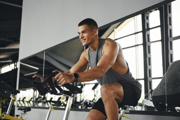 Happy caucasian athletic man smiling while cycling on stationary bike at gym fitness. Fitness and health care concept.