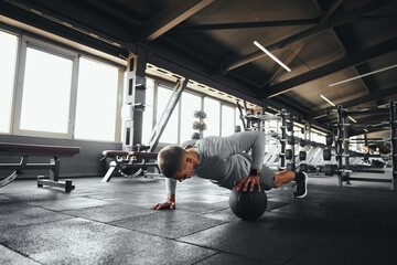 Fitness man doing push up exercise with one hand on medicine ball during intense fitness workout in...