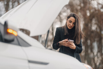 Businesswoman using smartphone near broken car with open hood
