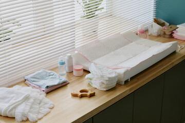 Clean and organized baby changing station with diapers, wipes, clothes, and changing pad arranged...