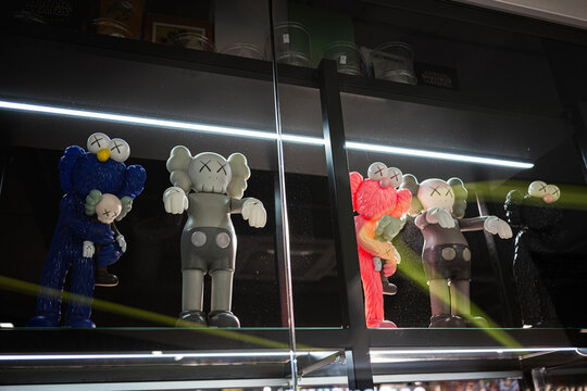 Collection of colorful collectible KAWS art toys displayed on a glass shelf at night