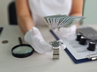 Person evaluates luxury watch while holding cash at a desk for transaction concept