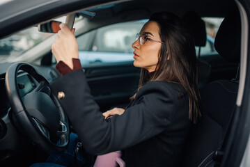 Businesswoman adjusting rearview mirror while driving car
