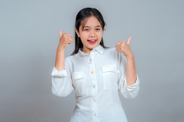 Cheerful young Asian woman smiling brightly and giving two thumbs-up while winking. Her...