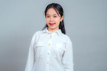 Cheerful young Asian girl with a playful expression, smiling confidently in a white shirt against a...