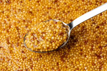 French Dijon mustard in a metal spoon, top view on mustard grains background. Gastronomy concept,...