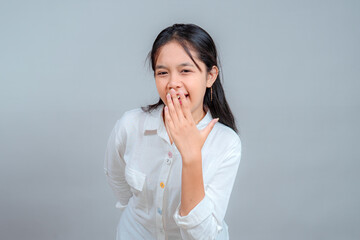 Portrait of a young Asian woman in a white shirt smiling shyly with one hand covering her mouth,...