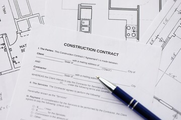Pen on residential construction agreement and planning blueprints of residential building project
