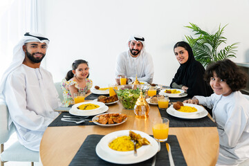 Happy arab family wearing emirati clothing spending time together at home - Middle-eastern parents and children bonding in modern apartment in Dubai