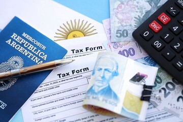 Argentine pesos money bills in big amount lies on table with pen, calculator, passport and tax forms
