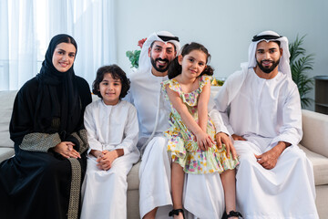 Happy arab family wearing emirati clothing spending time together at home - Middle-eastern parents and children bonding in modern apartment in Dubai