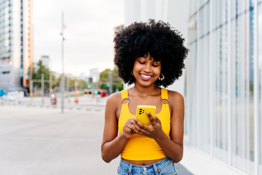 Beautiful young happy african woman with afro curly hairstyle strolling in the city - Cheerful black student girl walking on the street